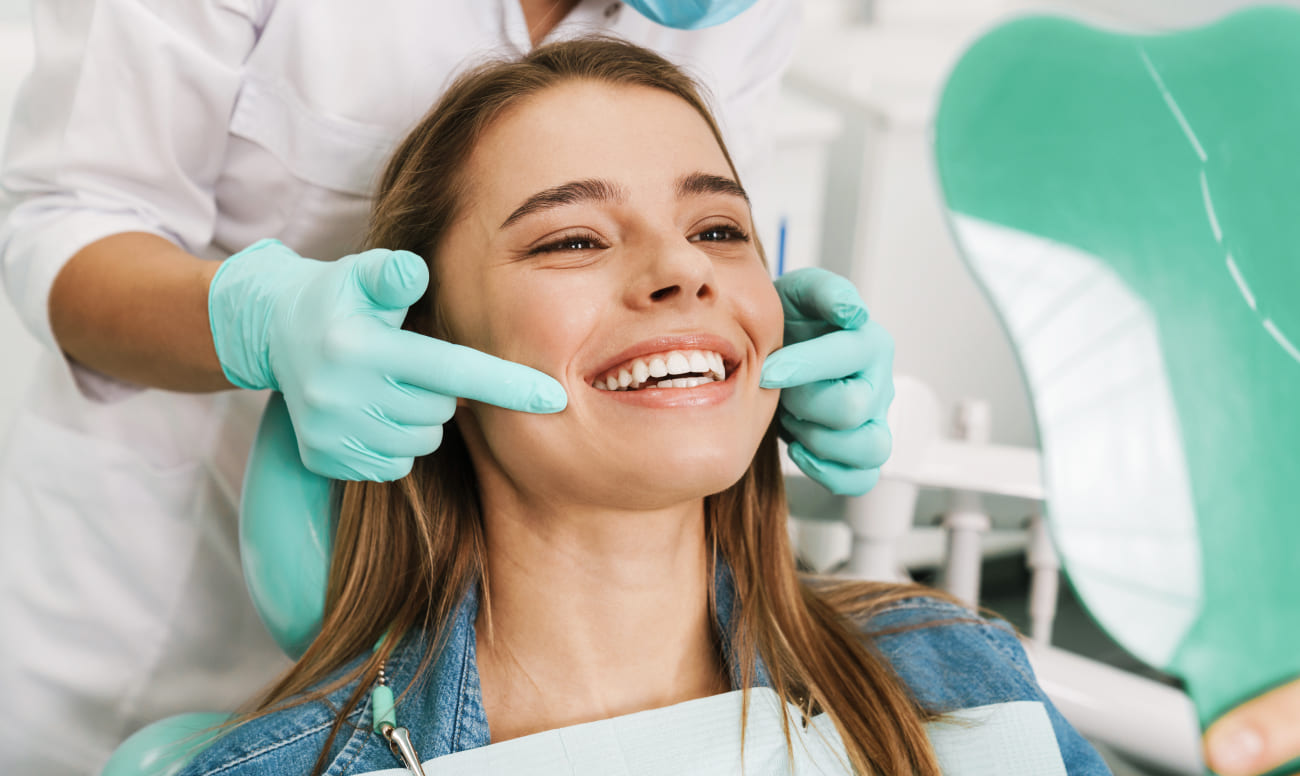 Фото улыбающейся девушки в стоматологическом кресле после реставрации зубов