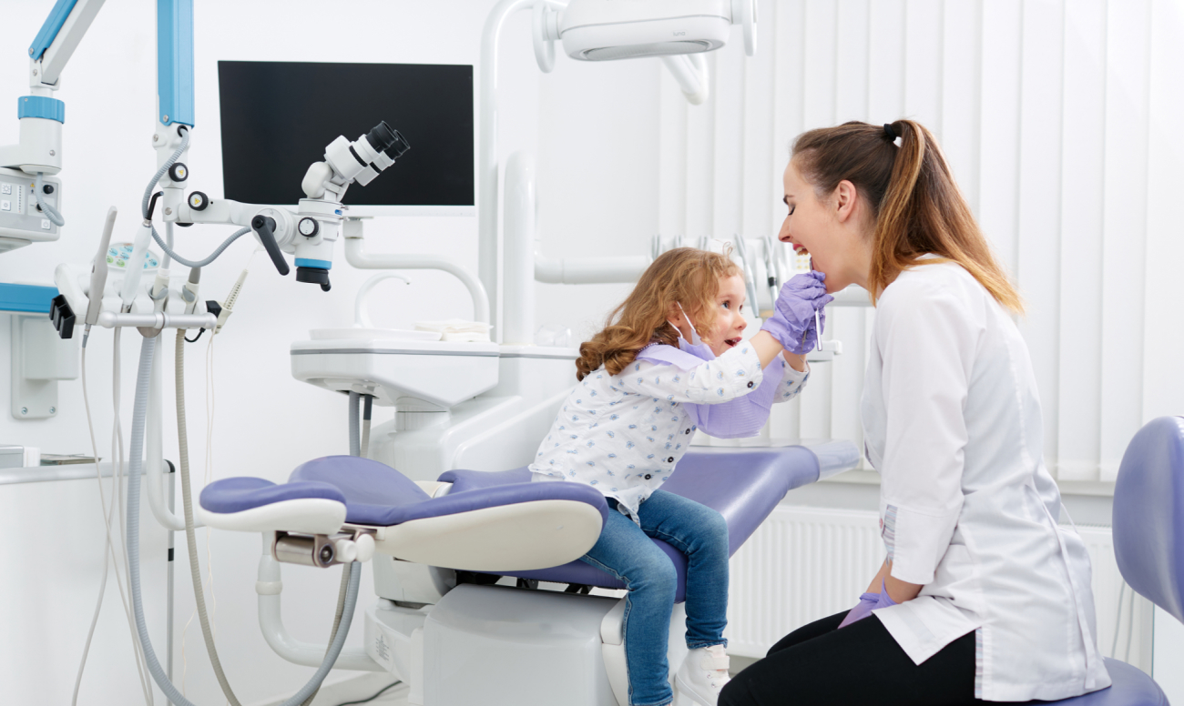 Фото ребенка на приеме у стоматолога, который адаптирует его к лечению