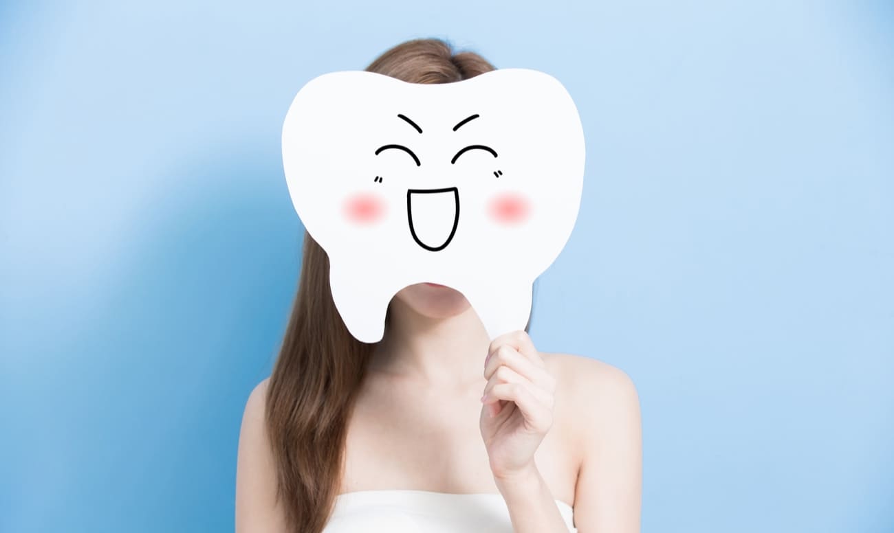 Фото девушки, закрывающей лицо вырезанным из бумаги зубом 
