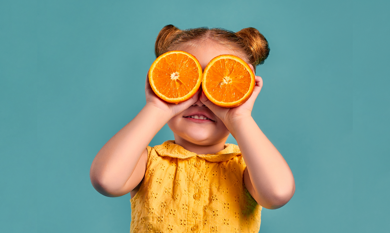 Фото ребенка, закрывающего глаза половинками апельсинов.